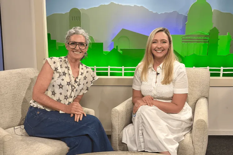 Two people sitting on chairs in a TV studio smiling at the camera.  