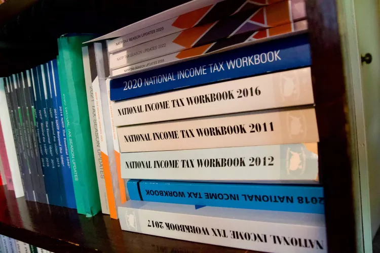 A stack of multicolored books on a bookshelf with the title "National Income Tax Workbook" on their spines. Each book has a different year after the title. 