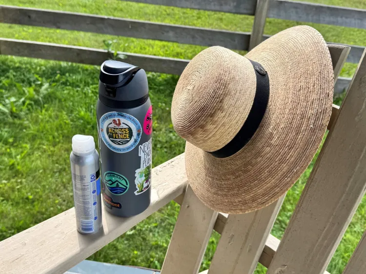 A sunhat, water bottle and silver sunscreen bottle are placed on a wooden lawnchair which is lit up by the sun.