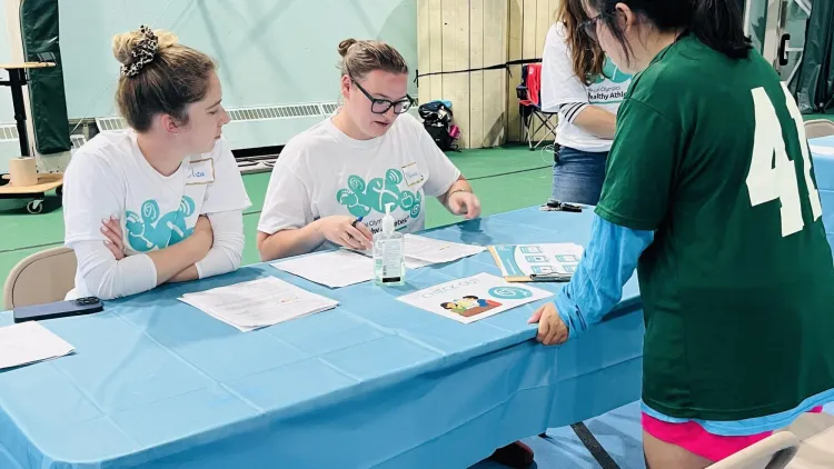 A participant speaks with volunteers at a registration table during a Special Olympics Healthy Athletes event.