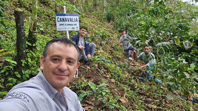 A man taking a selfie of three people sitting on a green hill with a sign. 