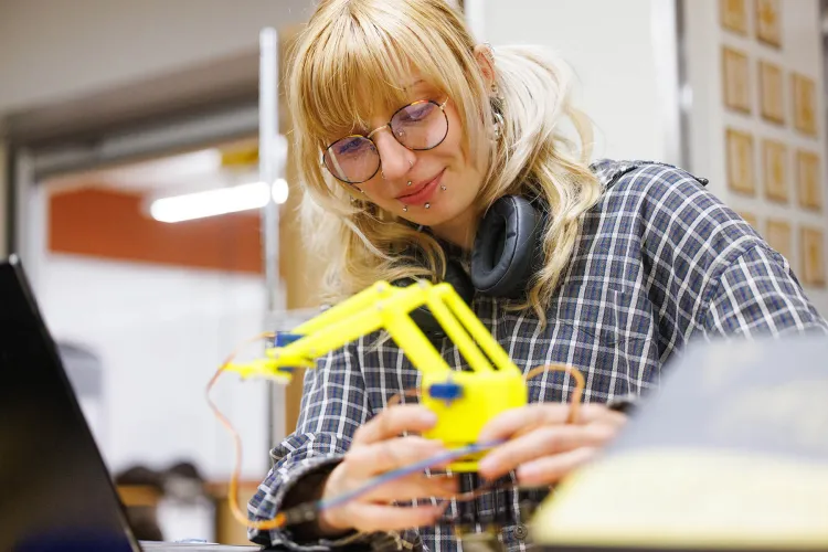 A student works on a robotic armature in a lab setting.