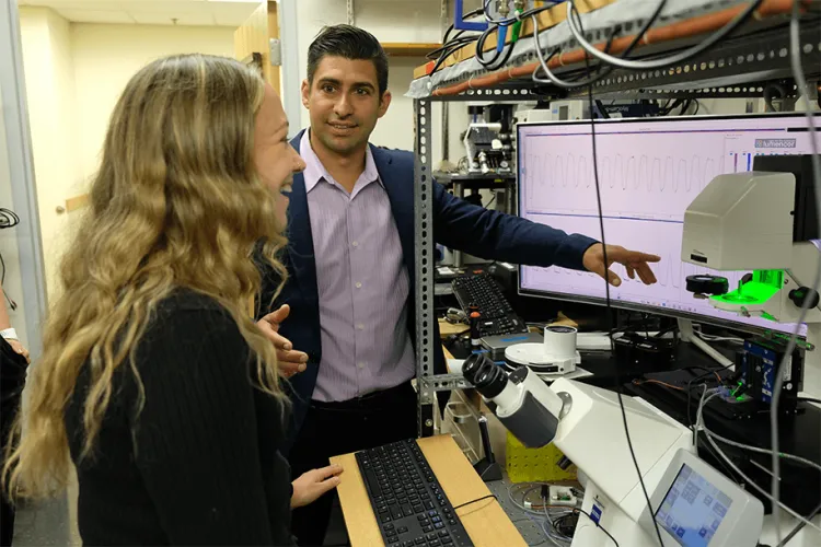 Person in a navy blue blazer shows a person with long blonde hair a graph on the computer in a laboratory setting.