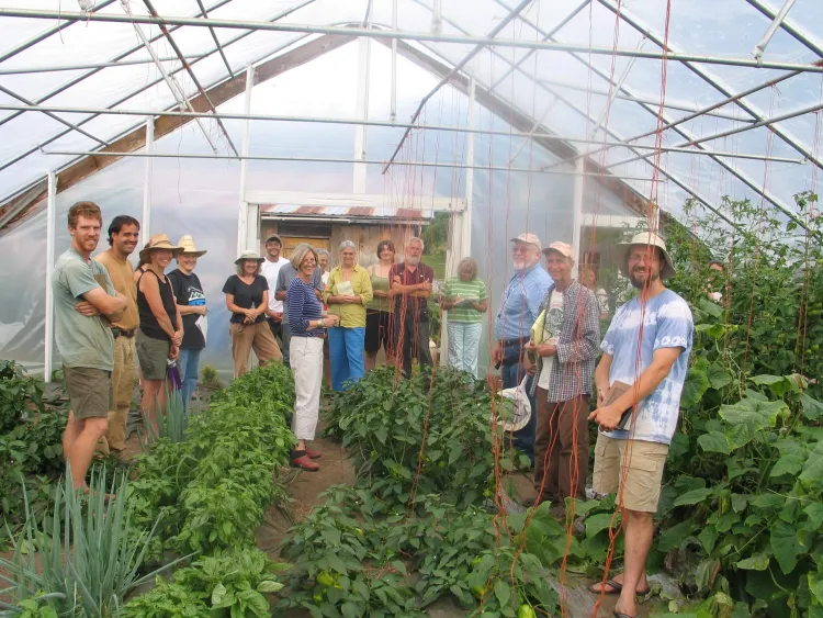A group of people look into a camera a smile while standing in a greenhouse among plants.