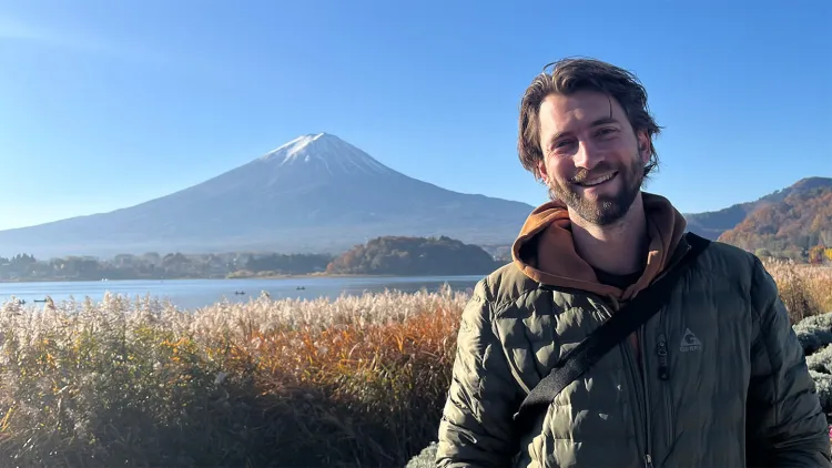 Person smiling outdoors with a mountain and lake in the background.