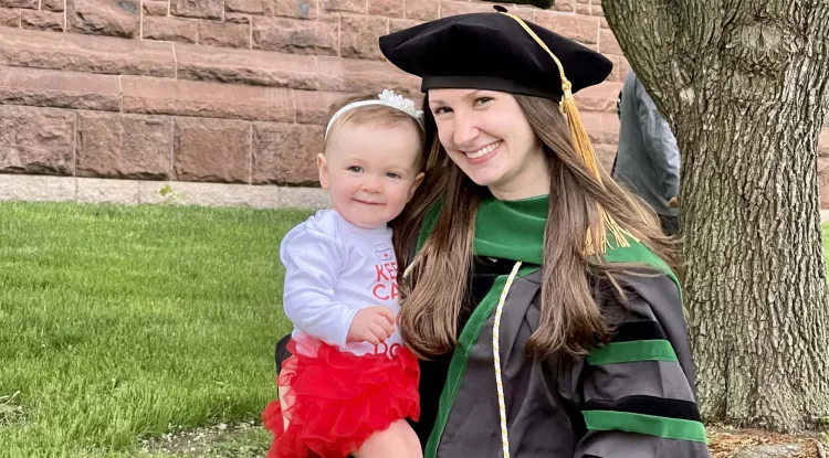 a medical school graduate in academic regalia holding a toddler 