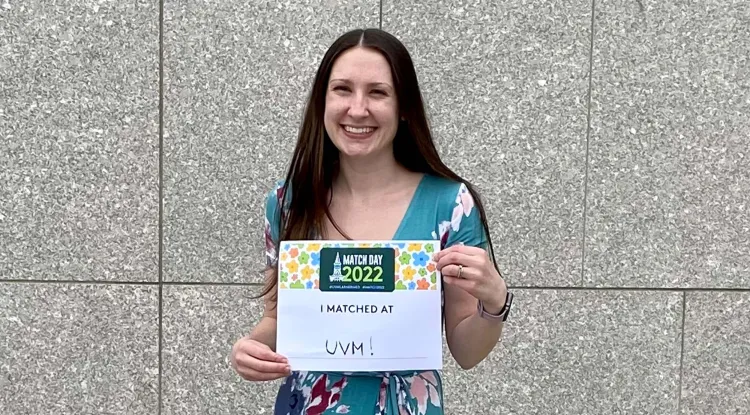 a person in a long floral dress holding a sign saying "I Matched At UVM!"