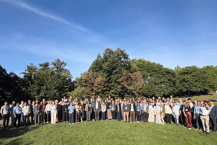 A large group of people outside in rows smiling for a group photo. 