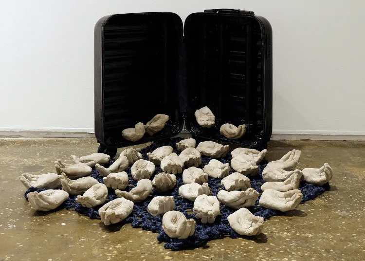 An array of cupped, cement hands spill out of an open suitcase. A sculpture by Nicolei Buendia Gupit.