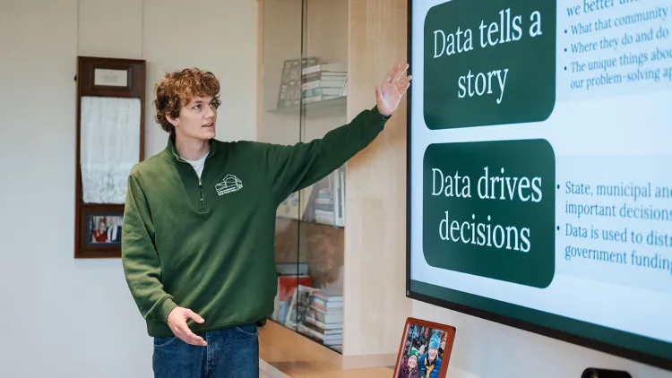 a student presents a slide about the importance of data. He gestures to a screen with phrases including "data tells a story" and "data drives decisions."