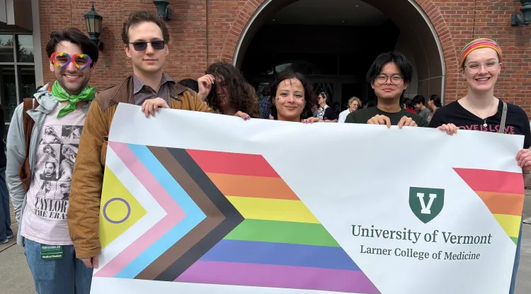 a group of people holding a rainbow-patterned banner reading University of Vermont Larner College of Medicine with the UVM V logo