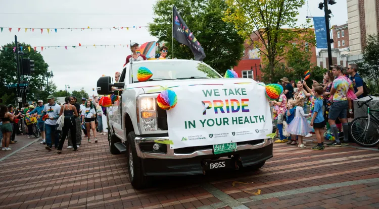 a truck with a banner on the front reading We Take PRIDE In Your Health, driving in a parade
