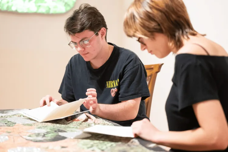 Two UVM students sitting at a table with open zines in their hands.