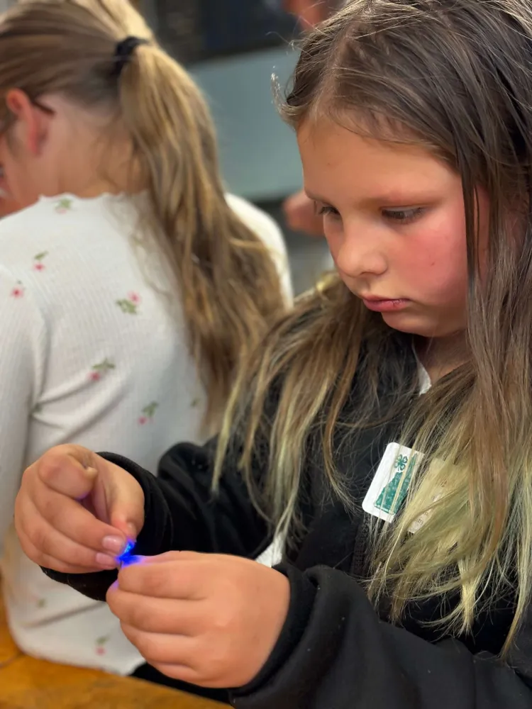A young girl holds something shining blue light on her fingers.