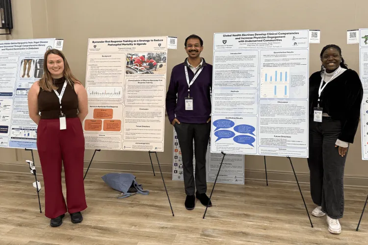 Three people smiling at the camera dressed nicely in front of scientific poster boards. 