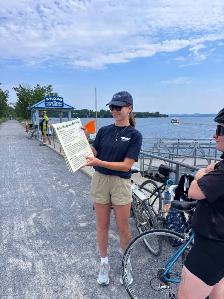 Hannah holds out a fact card and talks to a biker on the causeway