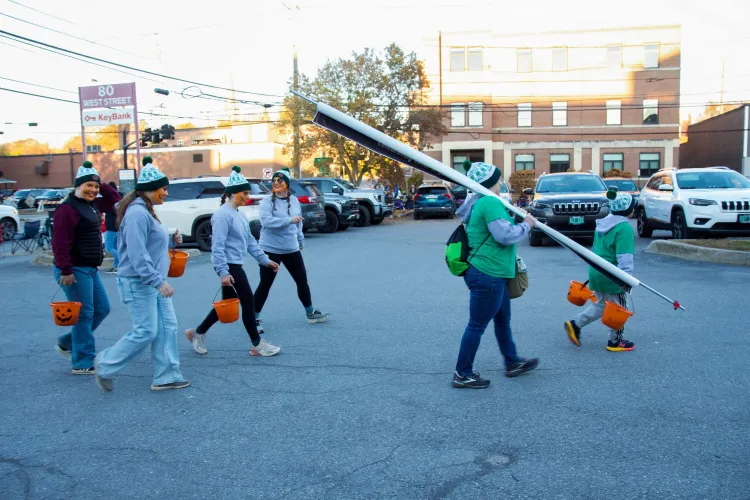 Two adults and several youth walk through a parking lot with pumpkin-shaped buckets and orange paint on their faces.