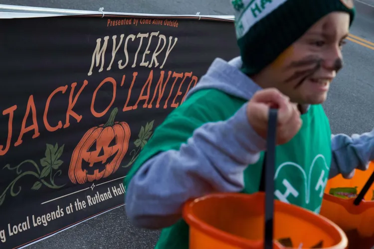 A banner reading "mystery jack o'lantern" with a carved pumpkin icon on it. A young boy in a green 4-H shirt holds up orange buckets in front of the banner.