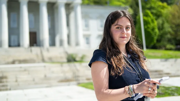 Kate Kampner stands outside the Vermont statehouse with her reporting pad and pen