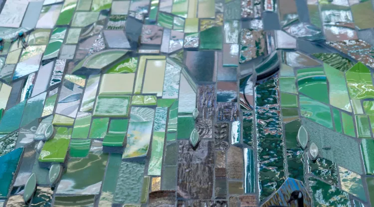 A vibrant mosaic composed of a variety of collected ceramic tiles, some glossy and others textured, as well as found objects, arranged in an abstract pattern.
