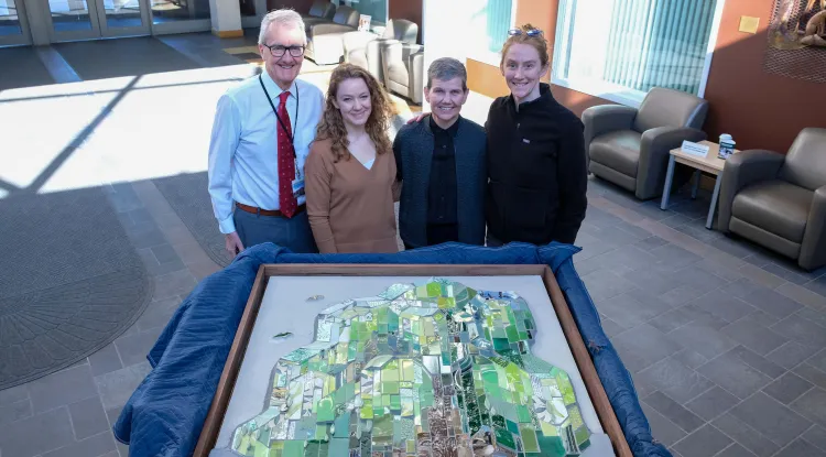 4 people standing next to a large mosaic in the process of being unpacked