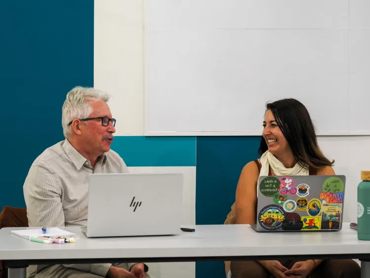 two people sit at a table behind lap tops