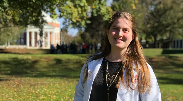 a person in a white coat standing outside on a college campus