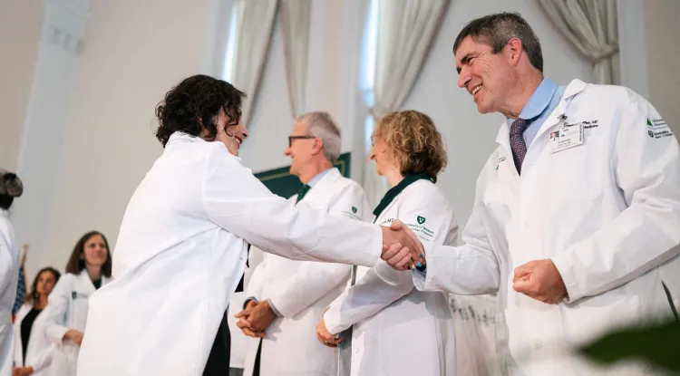 2 people shaking hands in a group of people wearing white coats on a stage