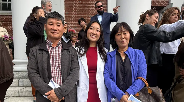 3 people standing in the foreground, with other people in the background, outdoors at an academic building