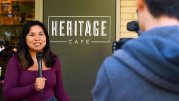 Students work together to film a news segment in front of Heritage cafe.