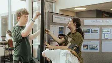 Students collaboratively setting up a display board in a campus building.