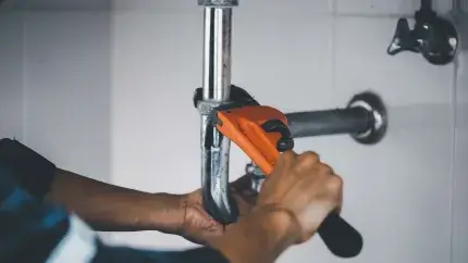 Hands using a wrench to tighten a leaky pipe.