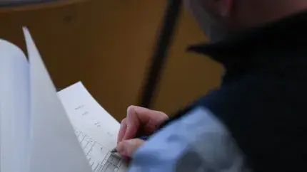 close up taken over the left shoulder of a person wearing a fleece vest who is holding papers and writing with a pen