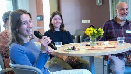 Student speaking into microphone at a table with Grand Friend and two other students