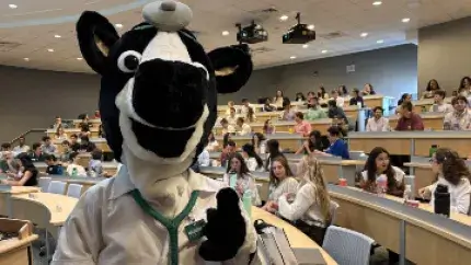 person in a a cow costume in an auditorium full of news students