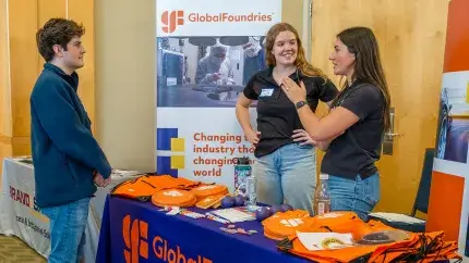 A student meets with two company representatives at their table during a career fair