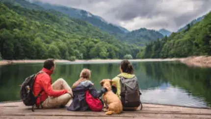 a family of three with a dog sit and watch mountains and a lake