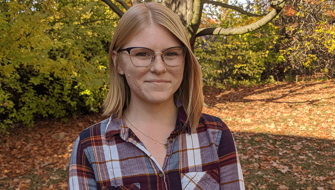 Sophia Trigg outdoors with fall leaves and trees in the background