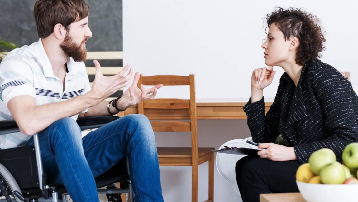 person in wheelchair talking with person seated in chair