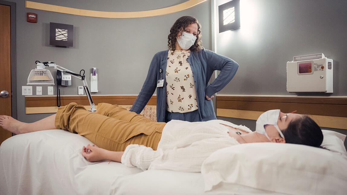 A patient lays in bed while a practitioner chats with her