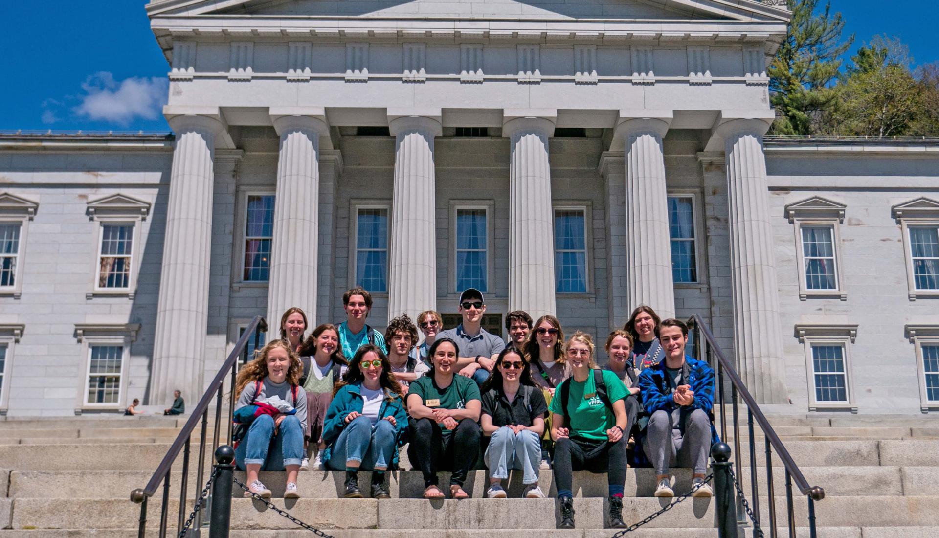 A group of students and staff pose for a photo on the steps of the Vermont State House.