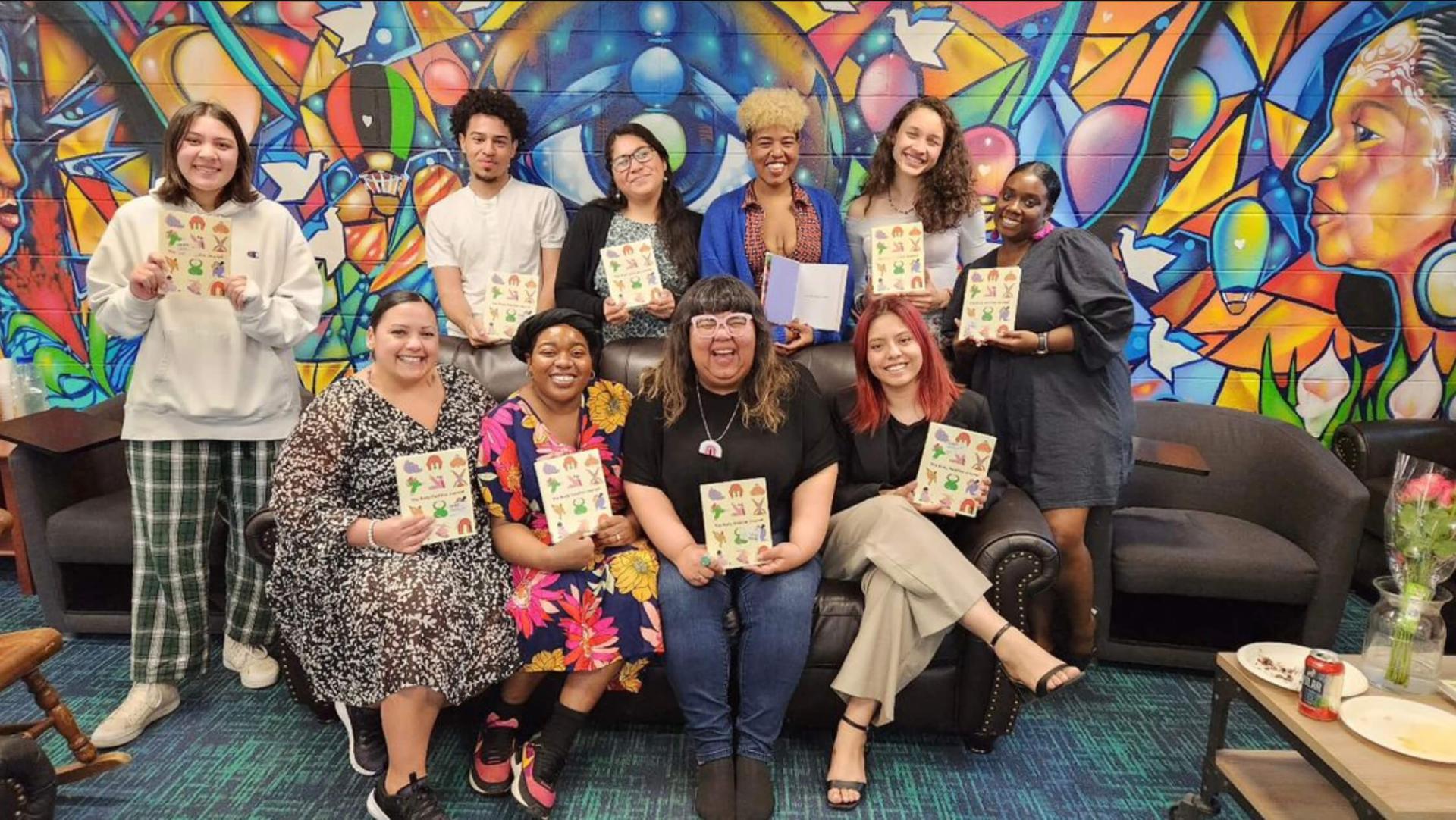 A group of students pose with Virgie Tovar (seated, third from left), all holding copies of Tovar's book "The Body Positive Journal"