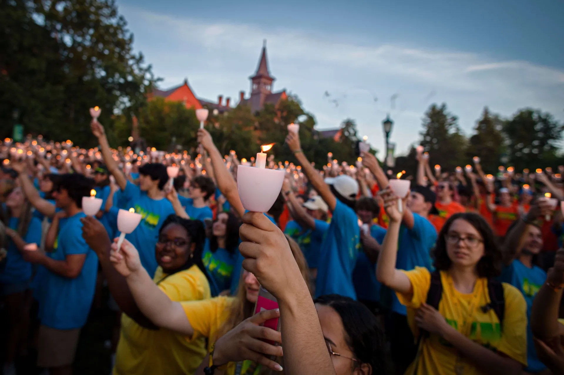 A large group of students look off camera while holding lit candles during a ceremony.
