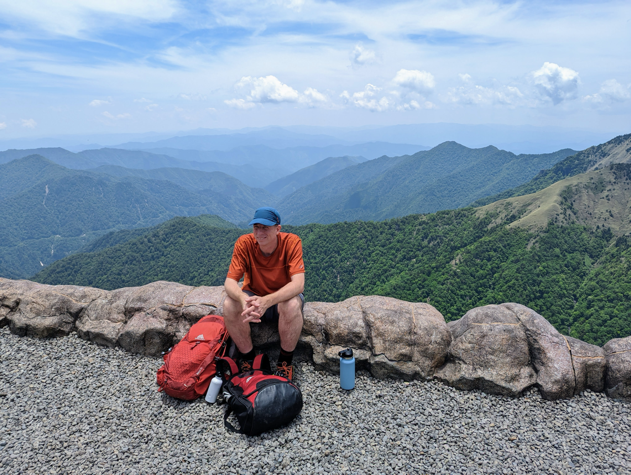 Man sitting atop a mountain with hiking gear