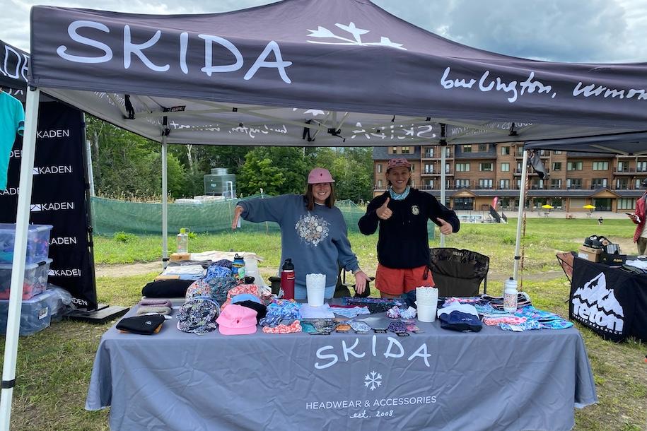 two women stand under a Skida farmer's market booth.