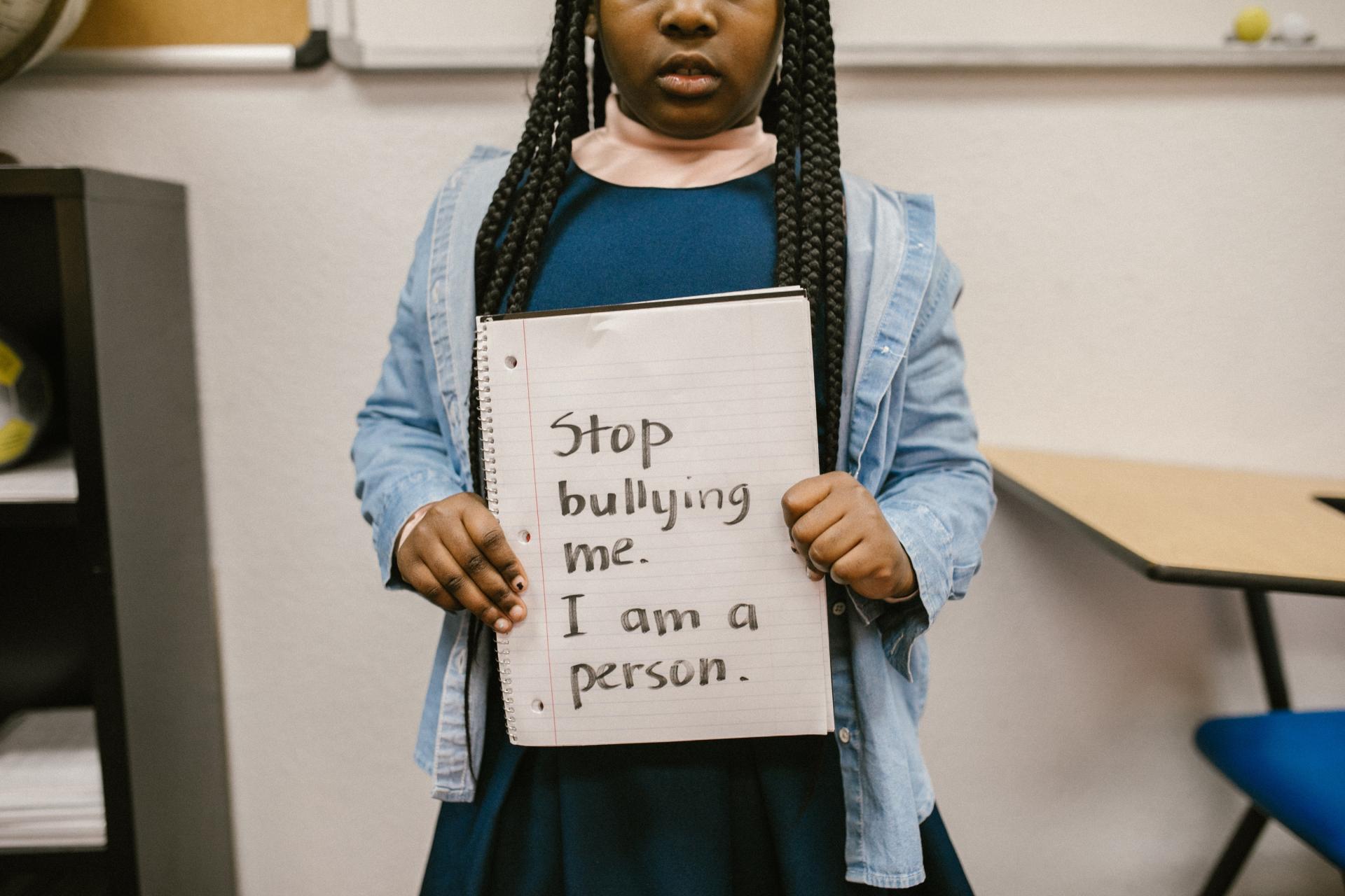 Black child holding a white piece of paper showing the words Stop bullying me, I am a person