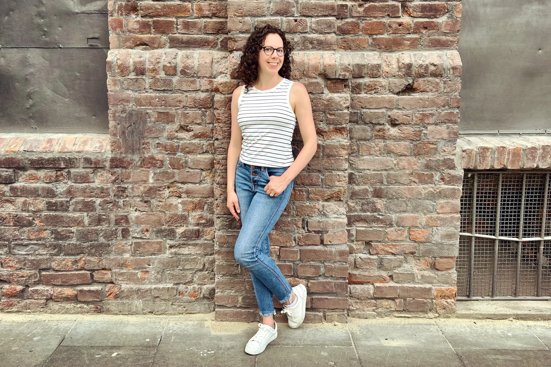 woman in jeans and sleeveless top standing in front of brick building