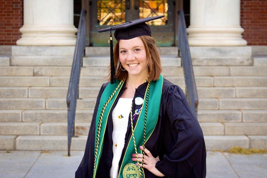 Claire Lennon dressed in UVM regalia in front of Waterman Building