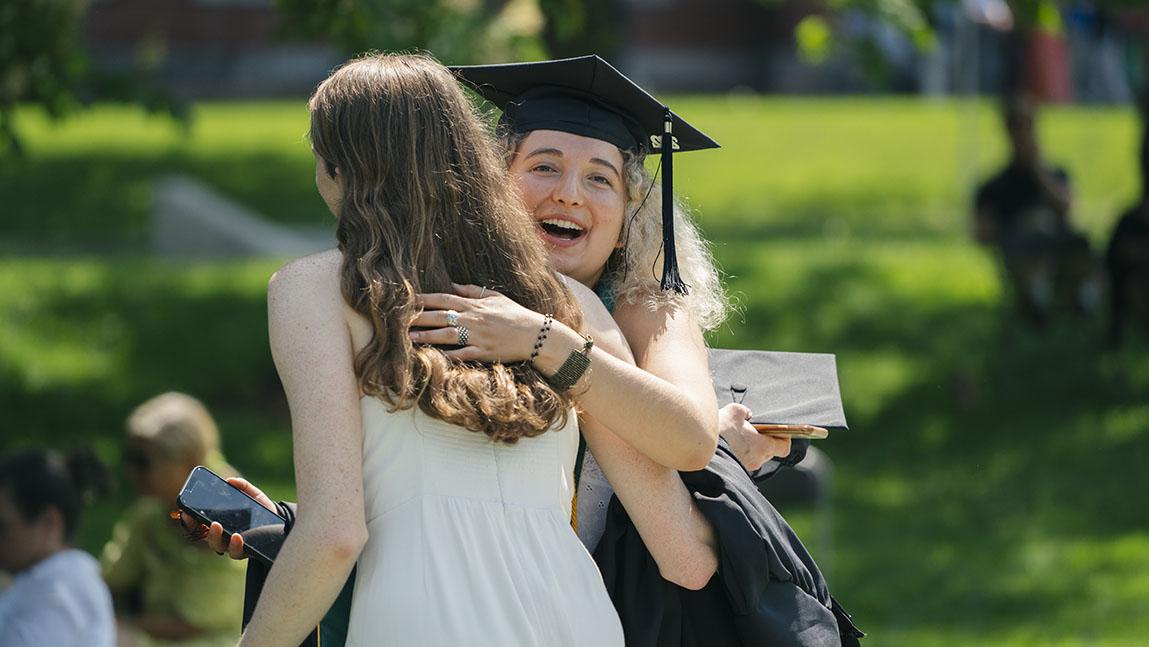 A woman hugs her friend while looking back to smile at the camera