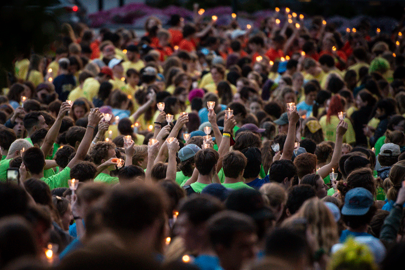 Thousands of students hold lit candles over head in unison.